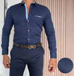 A man wearing a long sleeve printed shirt in blue with a geometric pattern, paired with trouser, standing indoor.