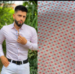 A man wearing a long sleeve printed shirt with a geometric pattern, with white trouser standing outdoors.